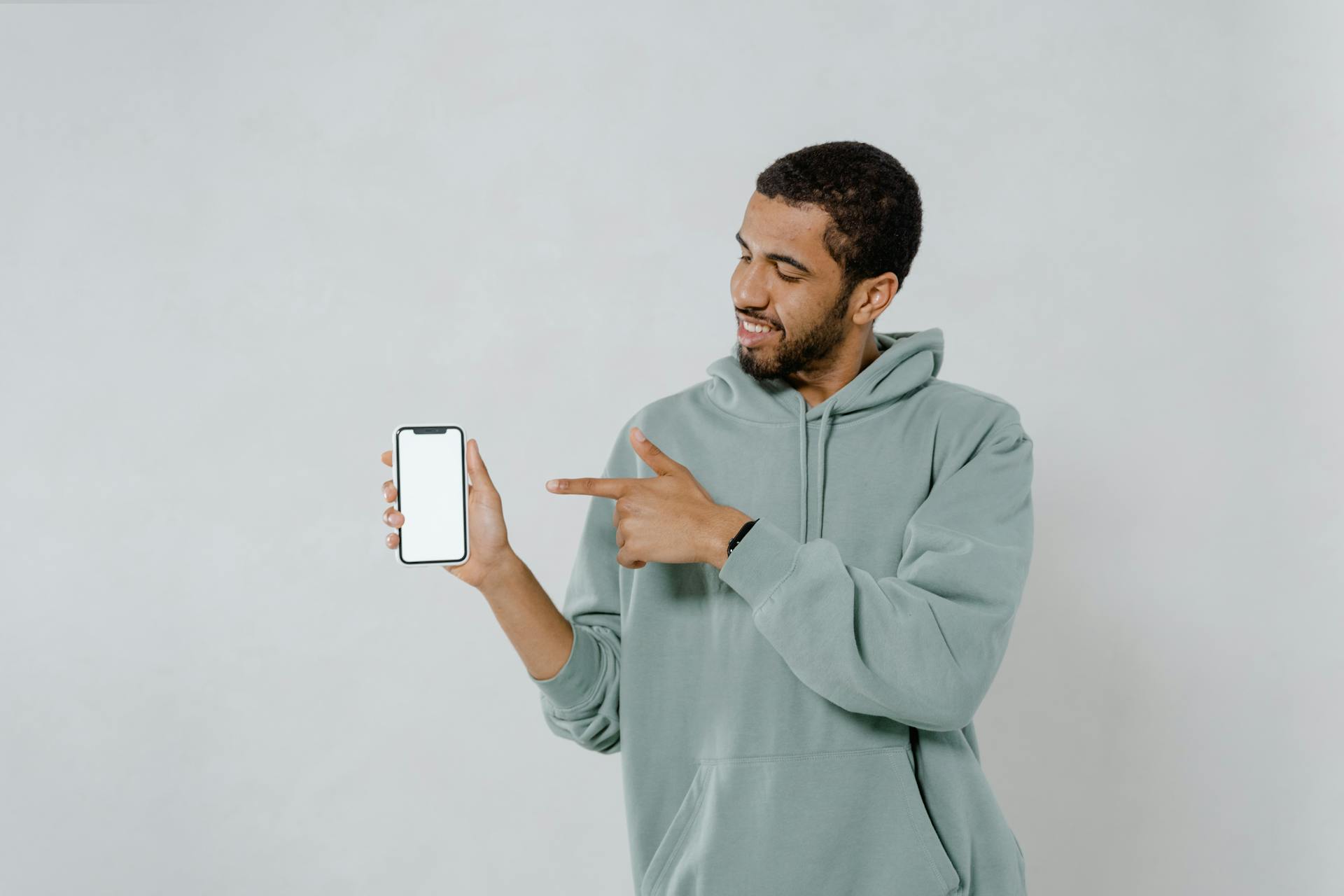 Photo of a Man in a Green Hoodie Pointing at a Mobile Phone