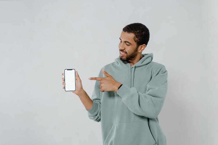 Photo Of A Man In A Green Hoodie Pointing At A Mobile Phone