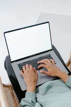 Person typing on a laptop from a high angle with visible keyboard and blank screen.