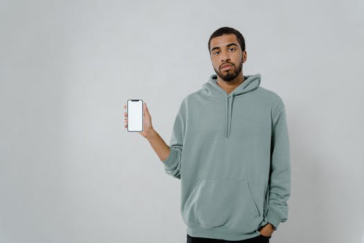 African American man holding a smartphone showcasing blank screen for mockup in studio setting.