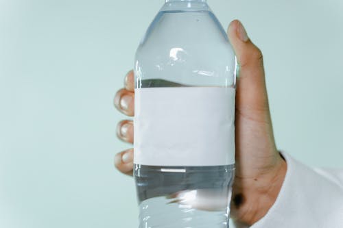 Free A clear plastic water bottle with blank label being held by a hand against a light background. Stock Photo