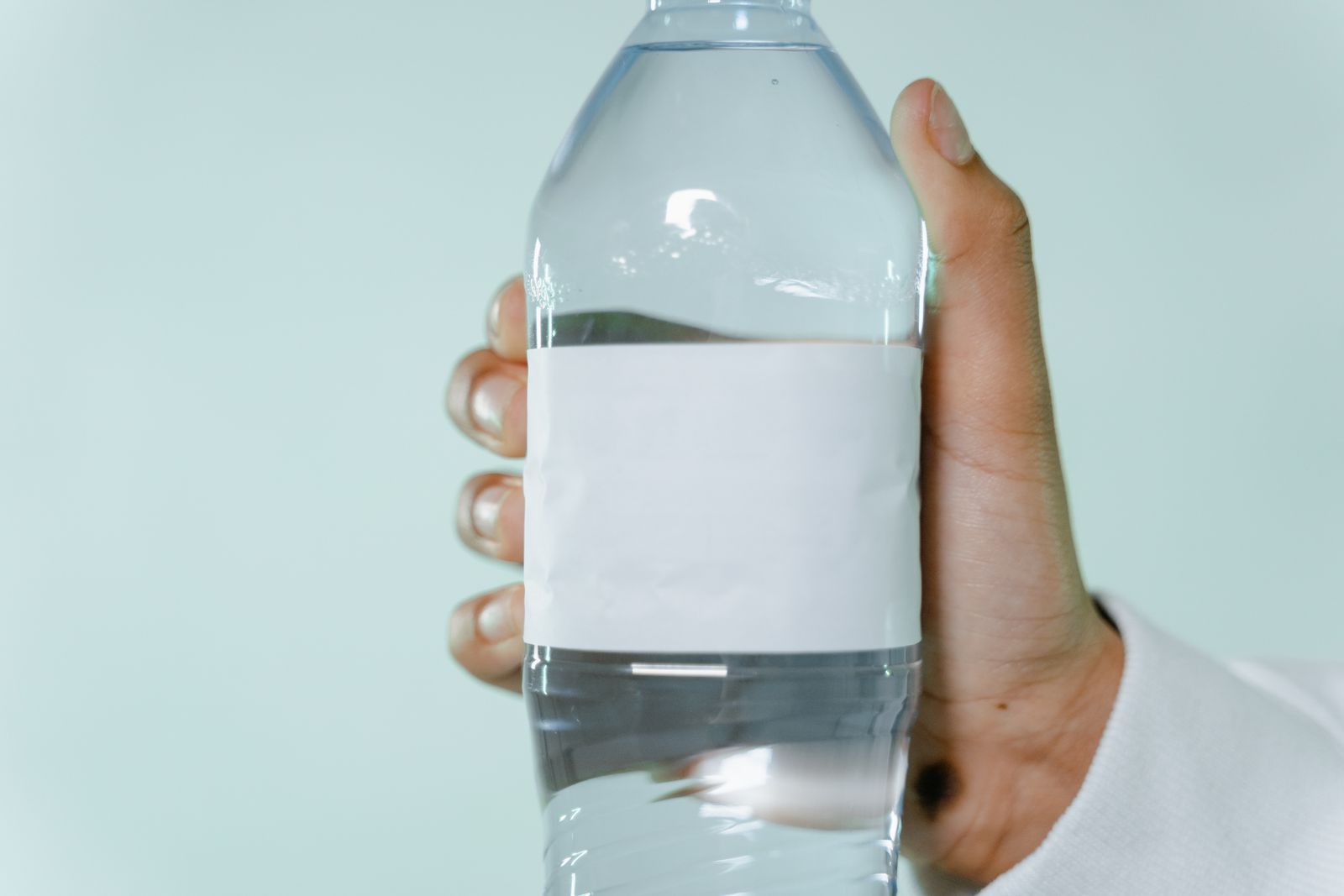 A person holding a plain, unbranded water bottle outdoors while traveling