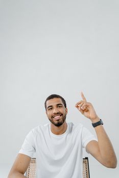 Confident young man in a white shirt smiling and pointing upwards on a white background.