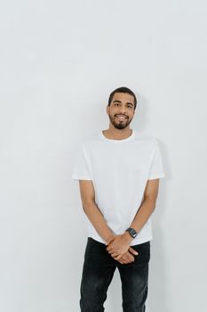 A cheerful man in casual attire stands against a plain white wall, creating space for text.