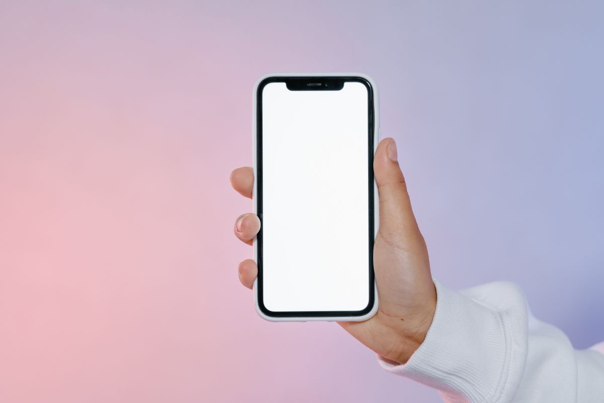 Close-up of a hand holding a smartphone with a blank screen against a soft pastel backdrop
