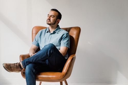 Free A man in casual attire sits contemplatively in a stylish armchair indoors. Stock Photo