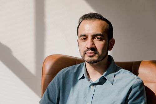 Free Sunlit portrait of an adult man sitting in a chair indoors, showcasing a serious expression. Stock Photo