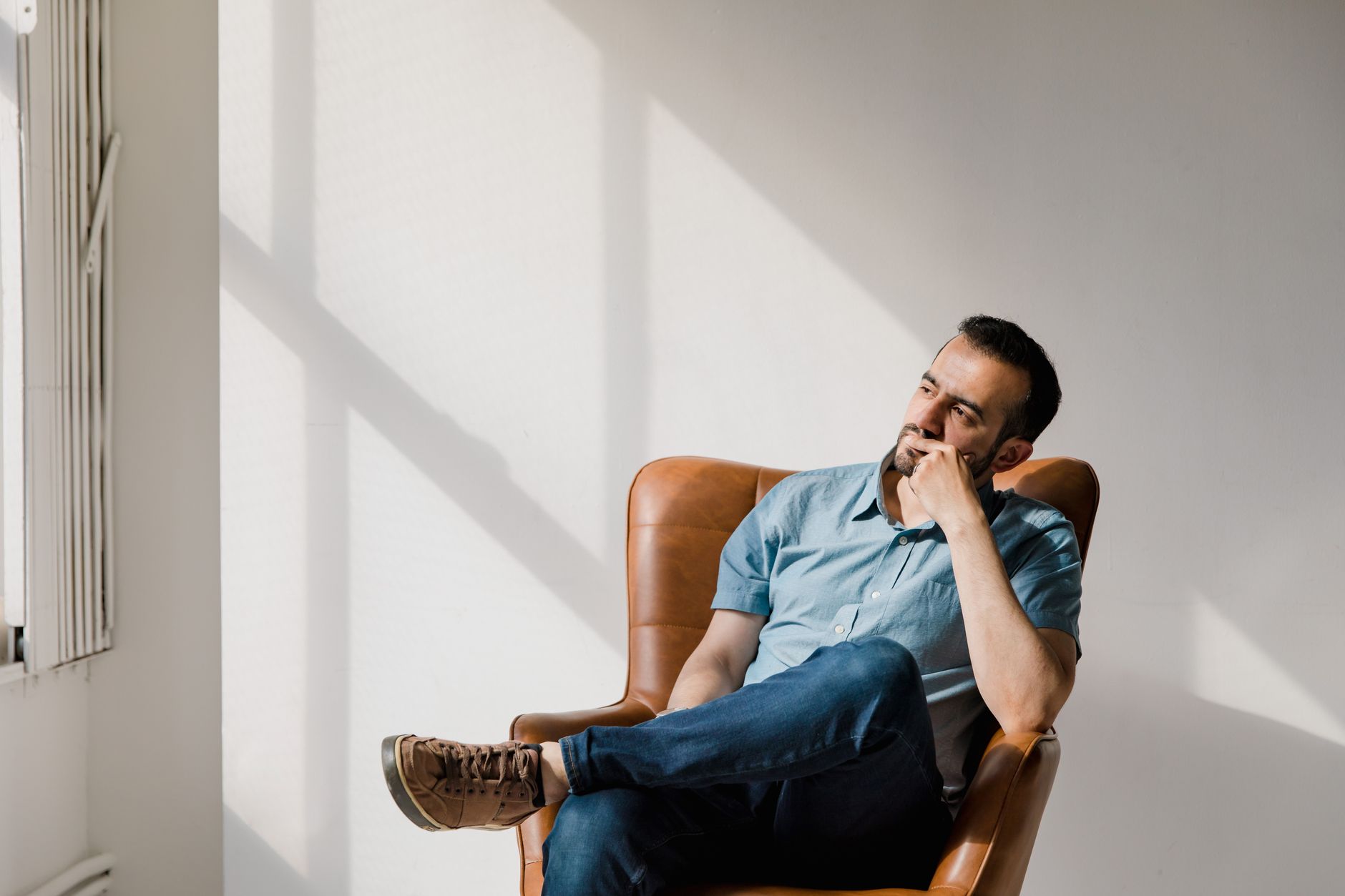 ivermectin dosing for long covid brain fog men over 50 — Man in casual attire sitting thoughtfully in a sunlit room, deep in contemplation.