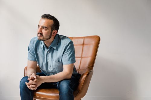 Free A thoughtful man in casual attire sitting on a modern leather chair indoors. Stock Photo