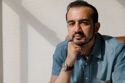Free A man with facial hair sits indoors, pondering with sunlight streaming in. Stock Photo
