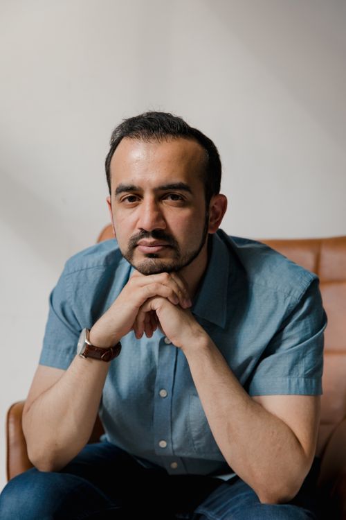 Free Portrait of a thoughtful man with a beard sitting indoors wearing a blue shirt. Stock Photo
