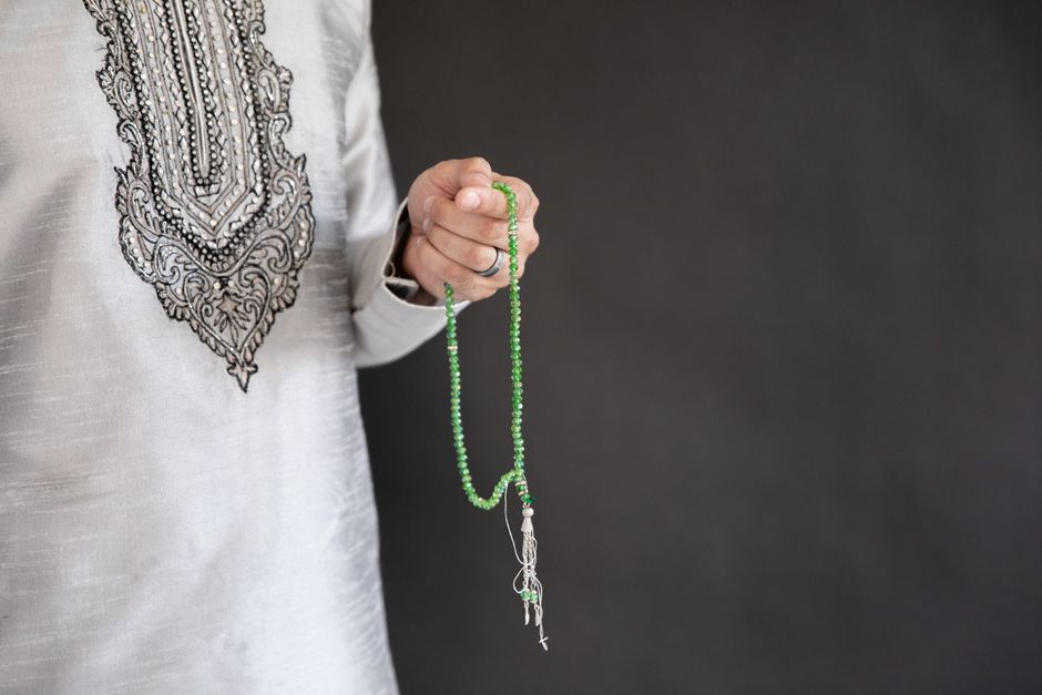 Close-up of a person holding traditional Islamic prayer beads against a dark background.