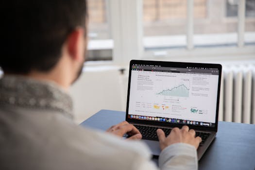 A person working on a laptop analyzing financial data in a bright indoor setting.