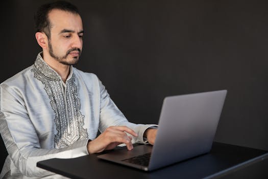 Man in traditional attire using a laptop indoors, focused and working.