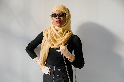 Free Fashionable woman in hijab and sunglasses exuding modern style with elegant pose against neutral background. Stock Photo