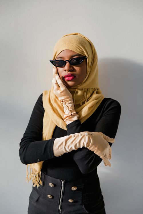 Free A fashionable woman in a hijab wearing sunglasses and gloves against a neutral background. Stock Photo