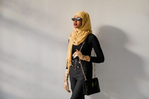 Free Fashionable woman in hijab wearing sunglasses and gloves against a neutral background. Stock Photo