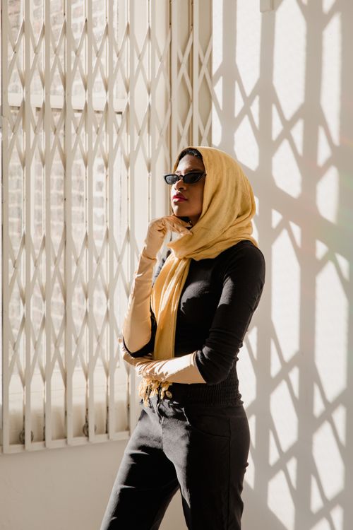 Free Fashionable woman in a yellow hijab and sunglasses in an indoor setting with shadow patterns. Stock Photo