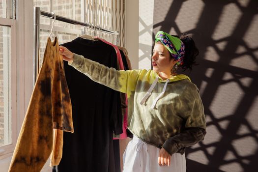 Young woman browsing clothing rack in a sunlit boutique. Fashion shopping concept.