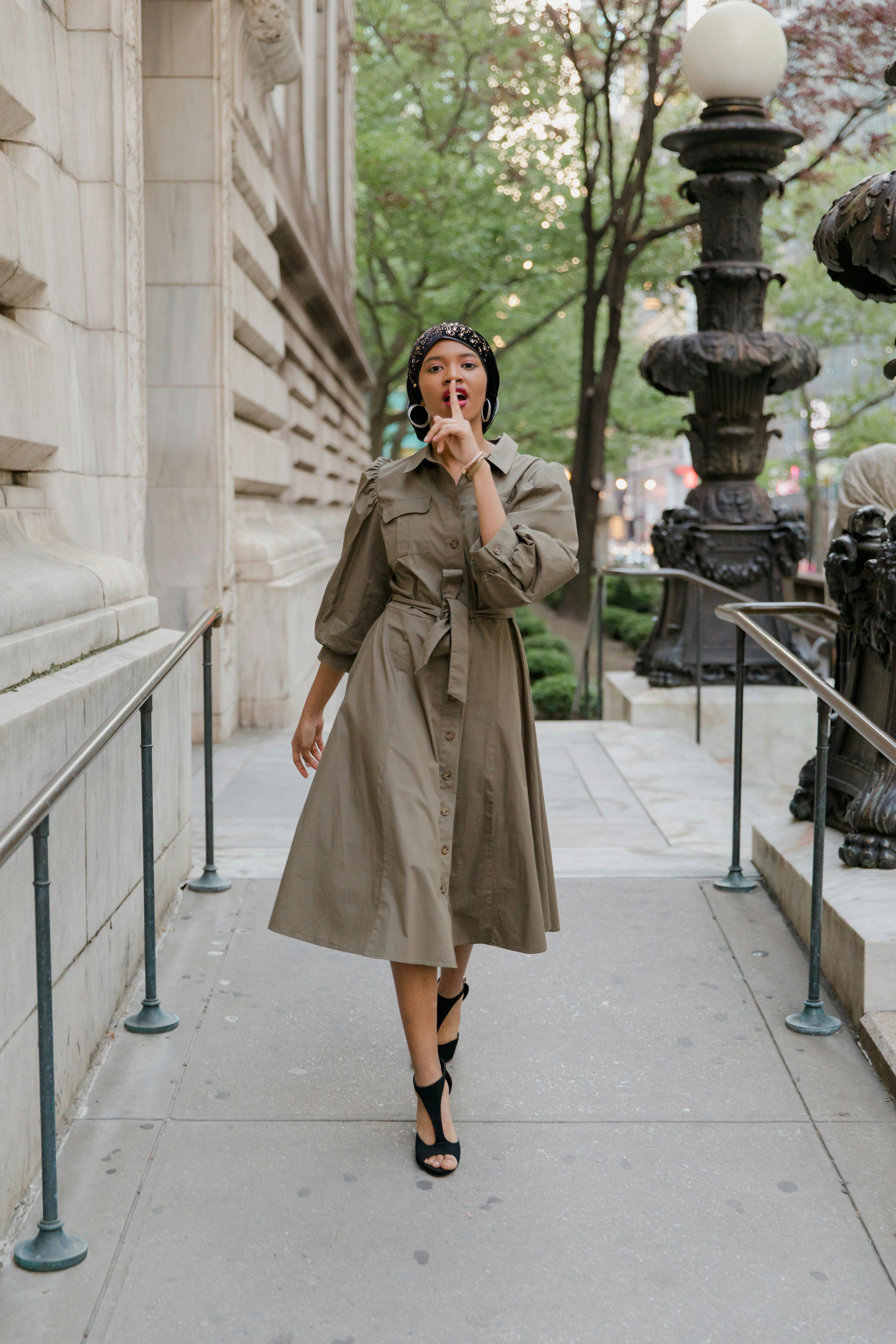 Woman in Brown Coat Standing Near White Concrete Pillar