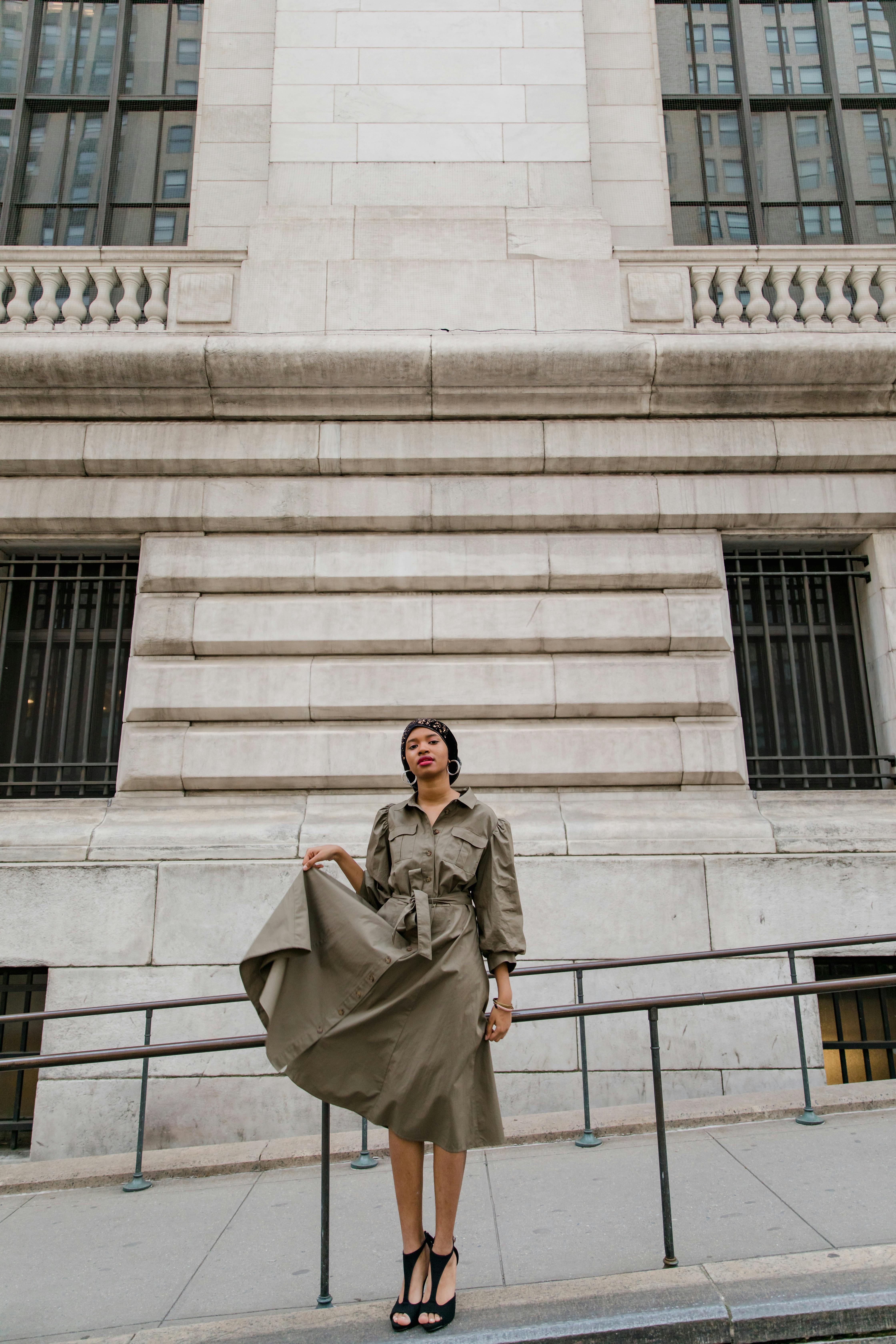 Woman in Brown Coat Standing Near White Concrete Building