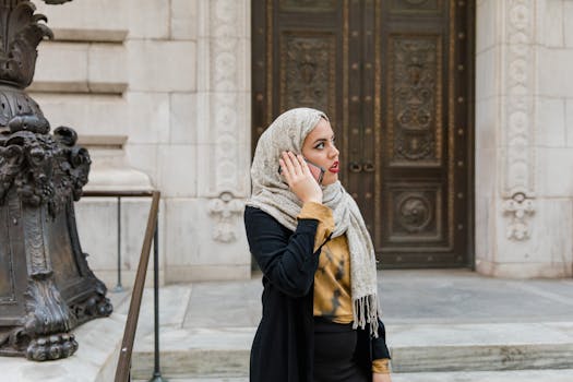 A woman in a hijab using her phone outside a historical building, capturing a modern lifestyle.