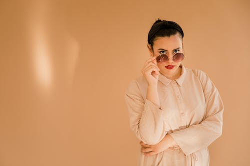 Stylish woman wearing sunglasses and a beige outfit, posing confidently indoors.