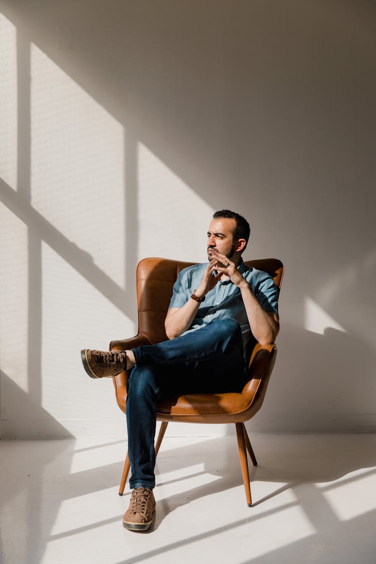 A Man Sitting On A Brown Leather Armchair