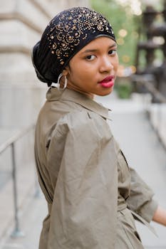 Young woman wearing a stylish headscarf and trench coat posing outdoors in a city setting.