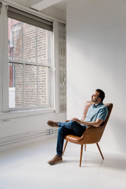 Man in Blue Dress Shirt Sitting on Brown Chair