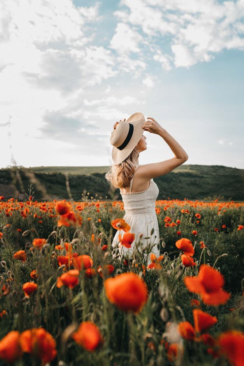 Female in hat standing in field with poppy flowers