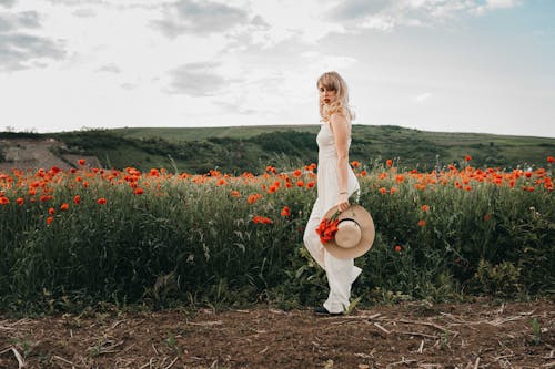 Stylish female standing against field with poppy flowers and green hills