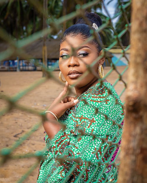 Photo of a Woman in a Green Top Posing Near a Chain Link Fence