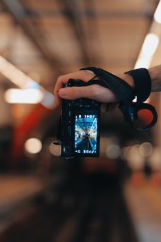 Close-up of a hand holding a camera capturing a blurred urban scene in focus.