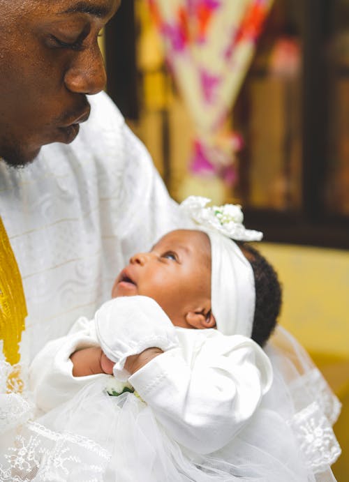 Photo of a Man in a White Shirt Carrying a Baby