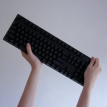 Hands lifting a black mechanical keyboard on a neutral background.