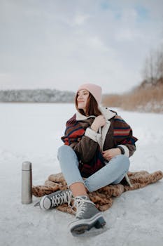 Caucasian woman sitting on snow, wearing warm clothing, enjoying a winter day outdoors.