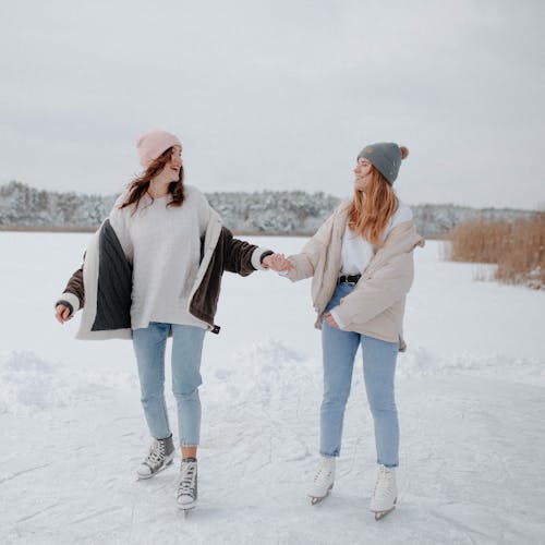 Two Women Standing On Snow Covered Ground With Ice Skates