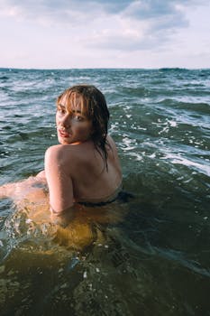 Young woman enjoying a refreshing swim in the ocean under a cloudy sky.