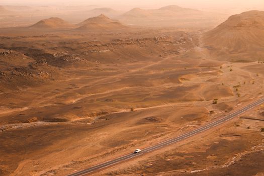 A lone car travels on a desert road in Tagounite, Morocco at sunset.