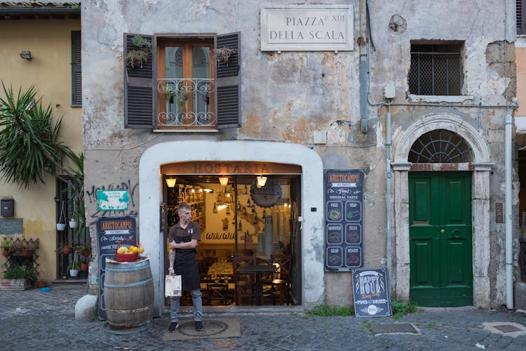 A Waiter Standing Outside The Restaurant While Holding A Menu