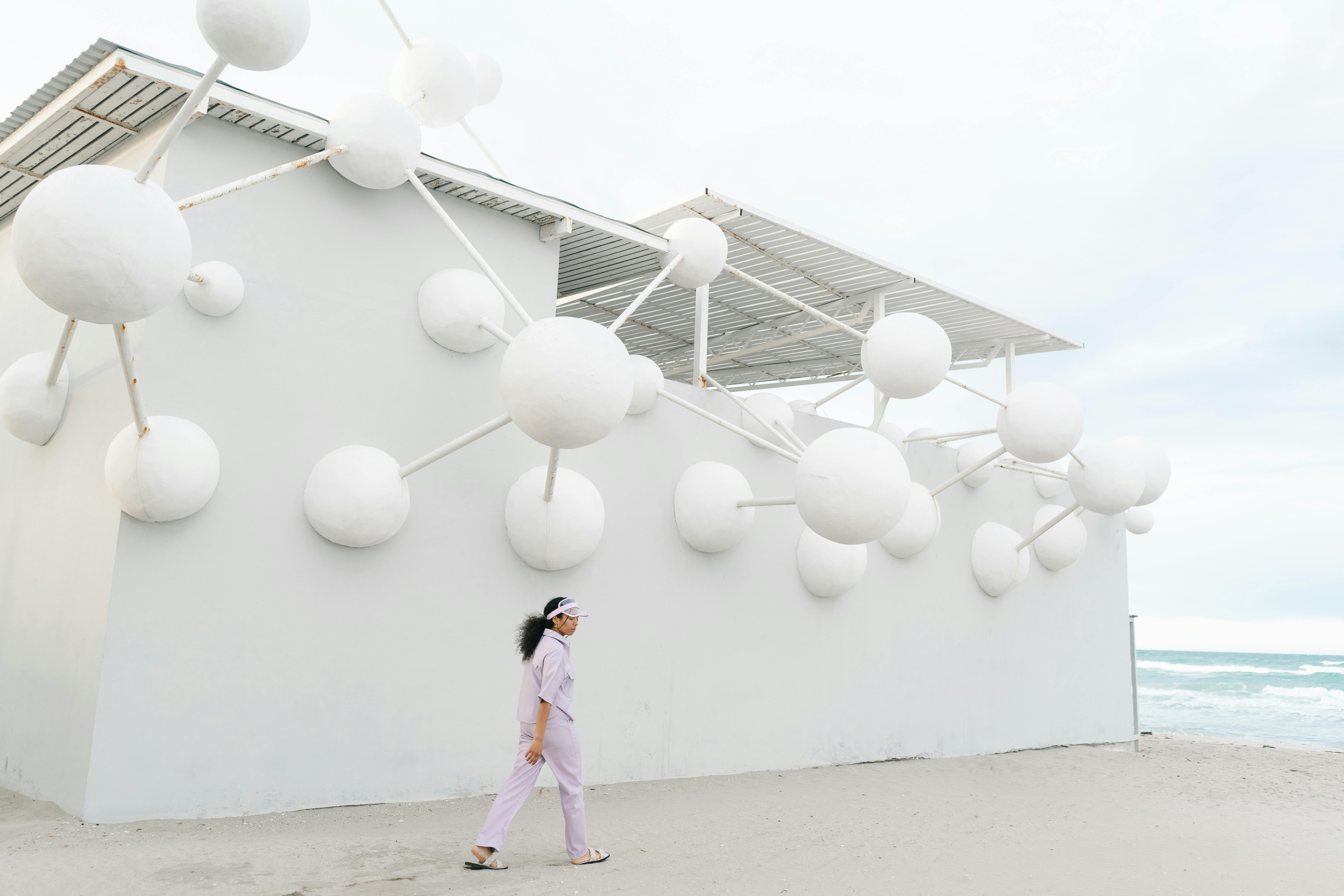 A woman walks past a futuristic beachside art installation with white spheres.