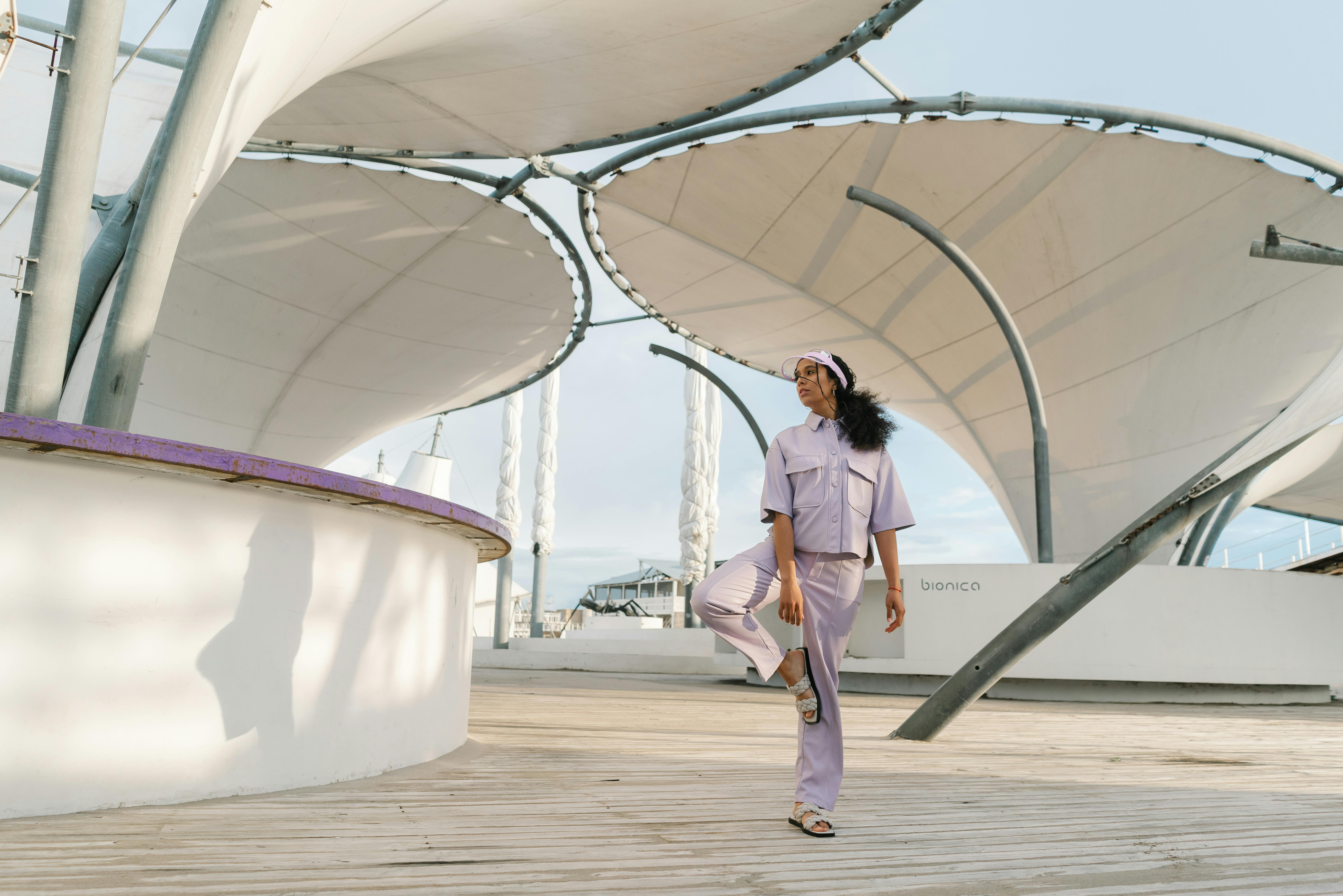A woman in a trendy outfit poses under modern structures outdoors, showcasing contemporary fashion.