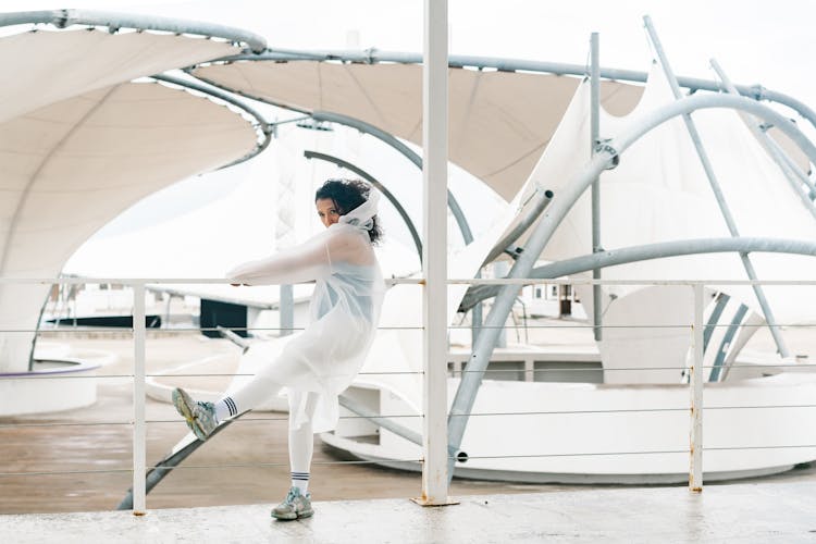 A Woman In White Raincoat Holding On To A Railing While Kicking