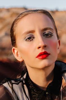 Close-up portrait of a fashion-forward woman with striking makeup set against an outdoor backdrop, showcasing modern style.