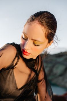 A stylish woman with bold makeup poses outdoors, showcasing modern fashion in natural light.