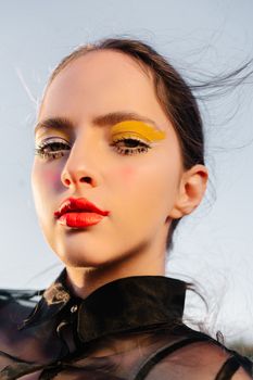 Striking portrait of a woman with bold lipstick and vibrant eye makeup in natural lighting.