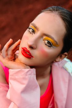 Close-up portrait of a woman with bold makeup, showcasing artistic eyelid and lip colors.