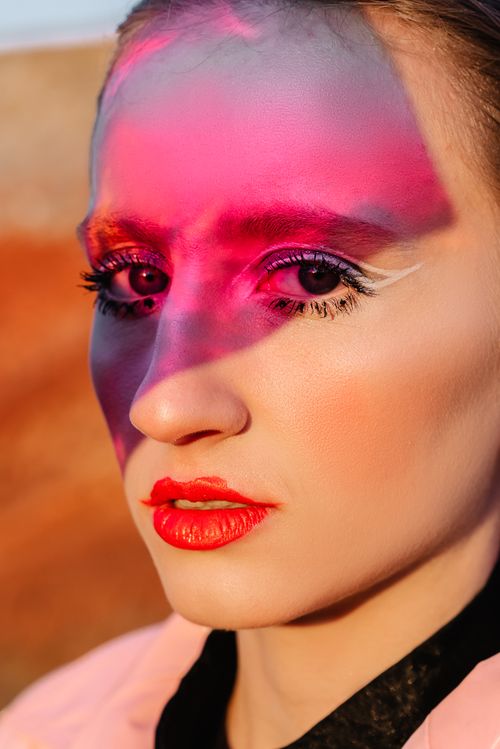 Free Close-up portrait of a woman with vibrant makeup in bold pink and red hues. Stock Photo