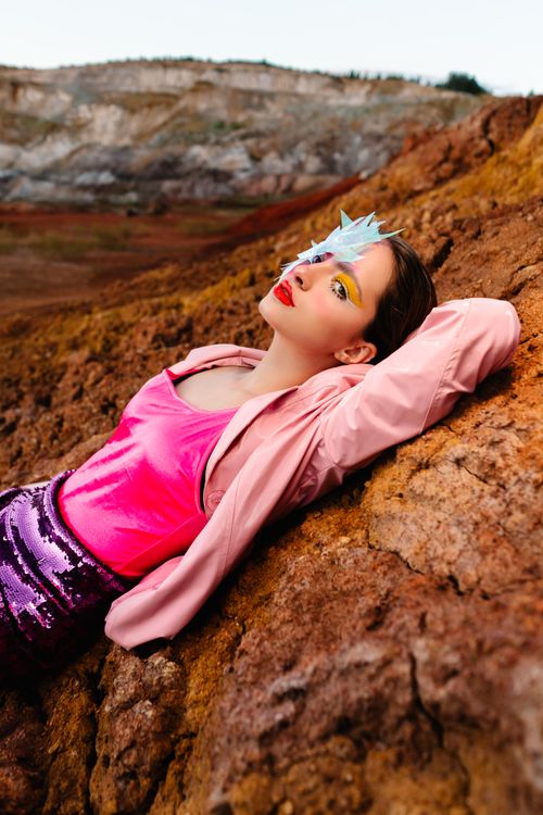 Free A stylish woman posing in colorful attire against a rocky landscape, showcasing bold makeup and fashion. Stock Photo